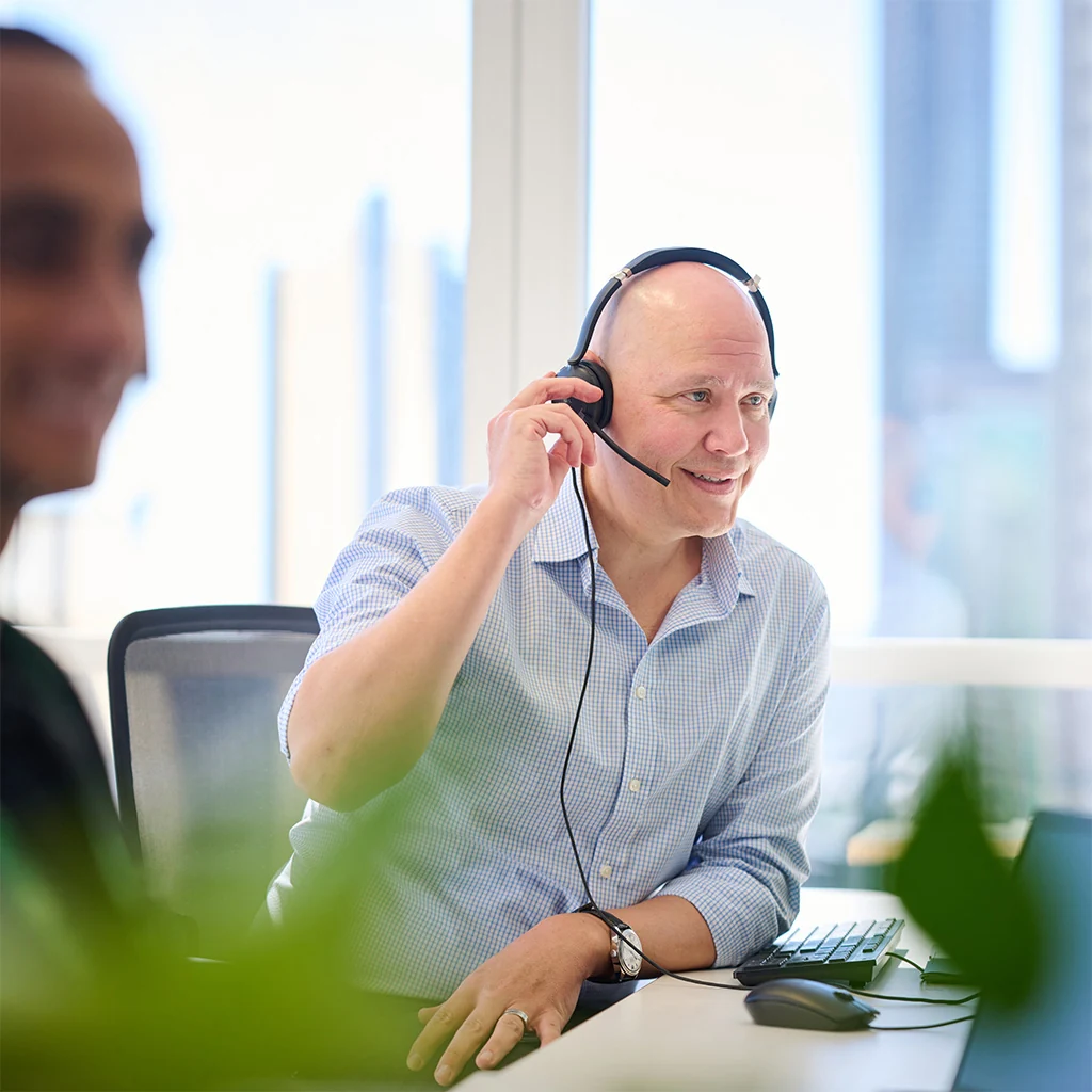 A man using a headset to talk on the phone while sitting at an office desk.