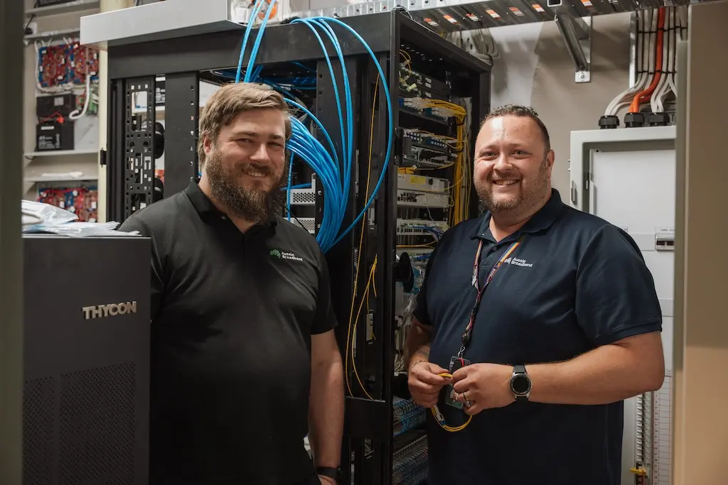 Two people standing next to a network rack